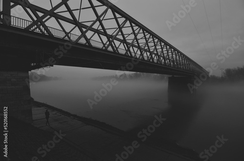 Silhouette of woman standing on the walkway under the bridge on a misty autumn night