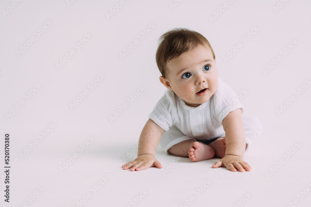 Side view of infant baby toddler in diaper and white bodysuit is crawling on all fours with his legs out, trying to stand up looking at camera over white background. Happy infancy and babyhood concept Side view of infant baby toddler in diaper and white bodysuit is crawling on all fours with his legs out, trying to stand up looking at camera over white background. Happy infancy and babyhood concept