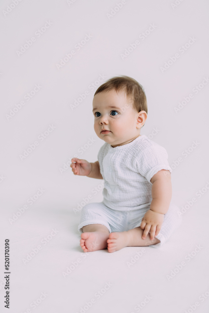Side view of infant baby toddler in diaper and white bodysuit is crawling on all fours with his legs out, trying to stand up looking at camera over white background. Happy infancy and babyhood concept Side view of infant baby toddler in diaper and white bodysuit is crawling on all fours with his legs out, trying to stand up looking at camera over white background. Happy infancy and babyhood concept