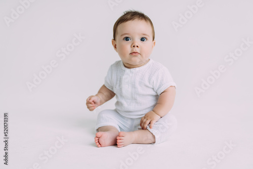 Small baby boy in a white bodysuit crawling on a white background