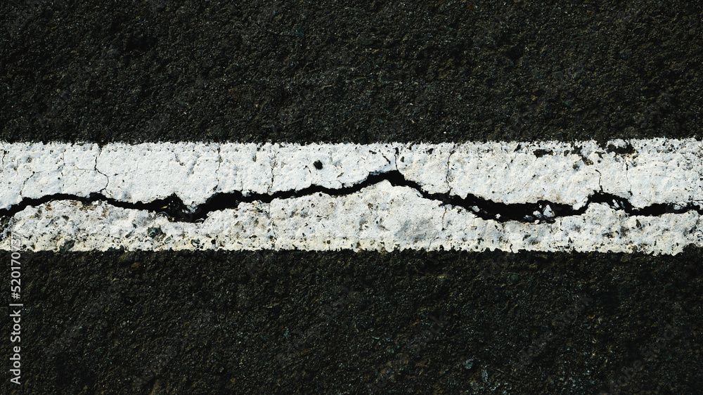 Fototapeta premium Worn white road line on cracked asphalt close-up