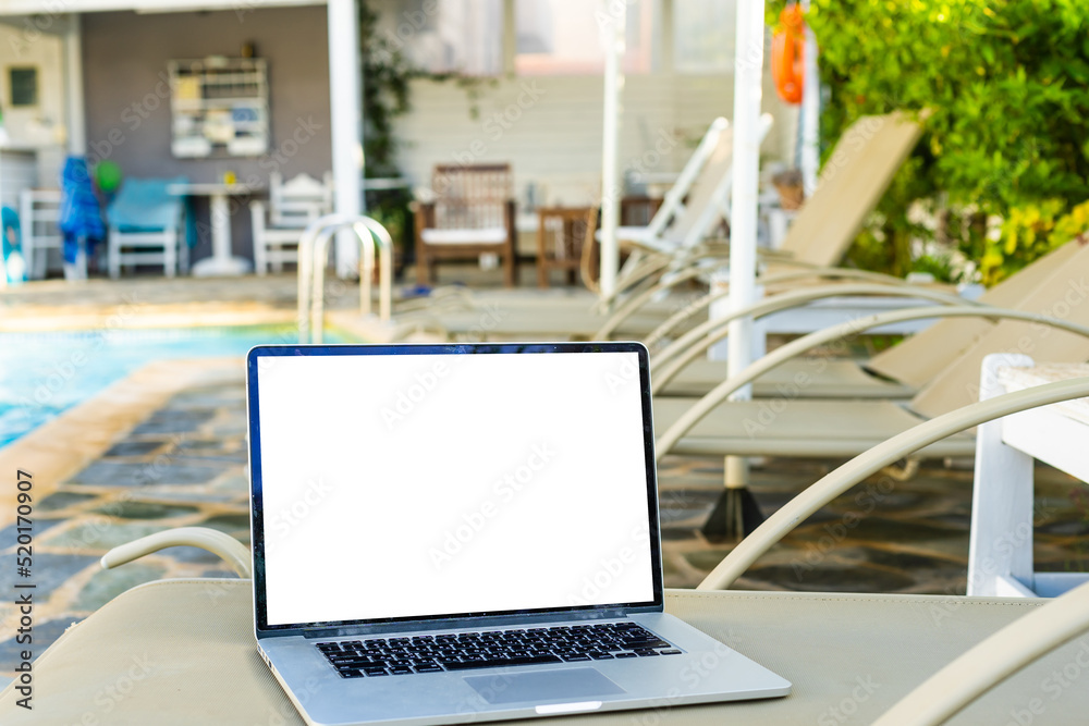 Fototapeta premium A laptop with an empty screen stands in the courtyard of a beautiful home garden, in Sunny weather.
