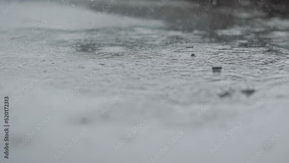 Slow motion closeup of summer heavy rain drops falling into puddles on asphalt