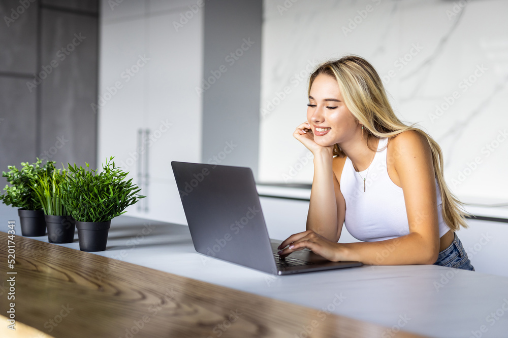 Happy young woman in the kitchen reading he news on her laptop Happy young woman in the kitchen reading he news on her laptop