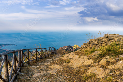 mountain landscape with a hiking trail leading to a mountain town and beautiful blue seashore far away