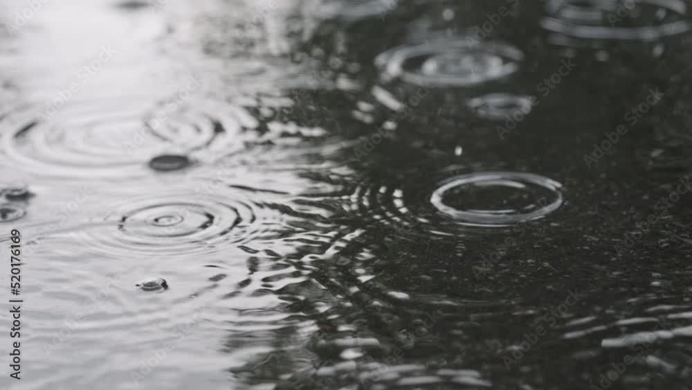 Slow motion closeup of summer heavy rain drops falling into puddles on asphalt