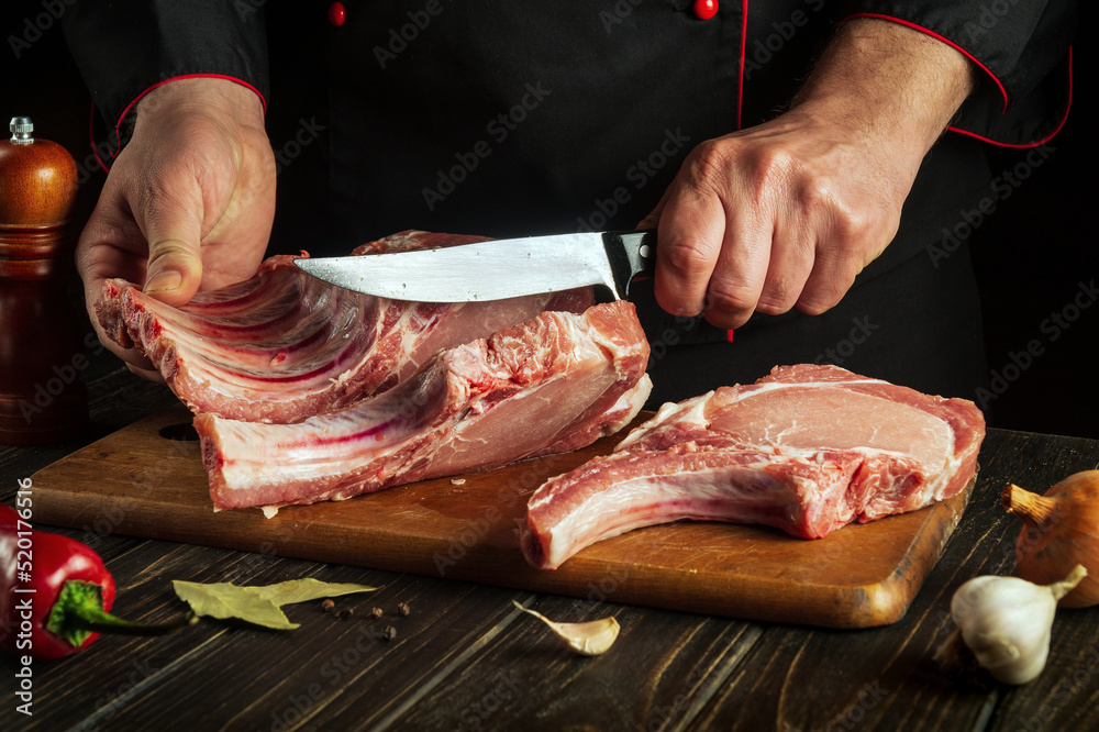 The hands of a cook or a butcher with a knife in the kitchen cut the ribs. Cooking a delicious grill for a restaurant or hotel
