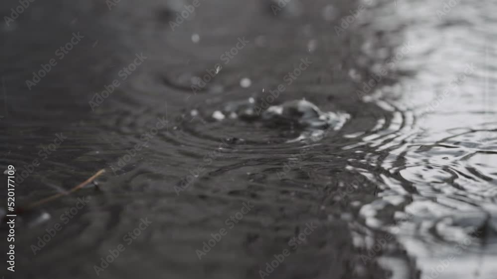 Slow motion closeup of summer rain falling into big puddle on asphalt Slow motion closeup of summer rain falling into big puddle on asphalt