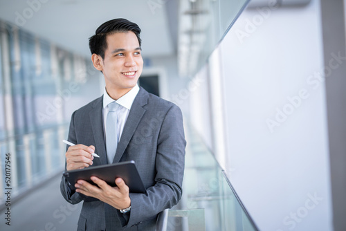Young asian business man holding a tablet looking away , smart business concept.