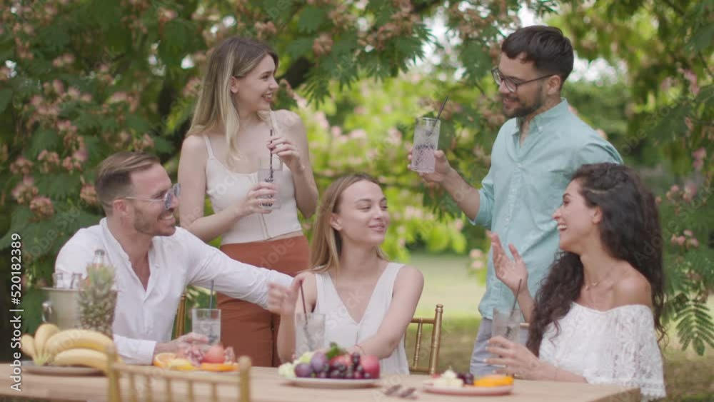 Group of happy young people cheering with drinks and eating fruits by the pool in the garden Group of happy young people cheering with drinks and eating fruits by the pool in the garden