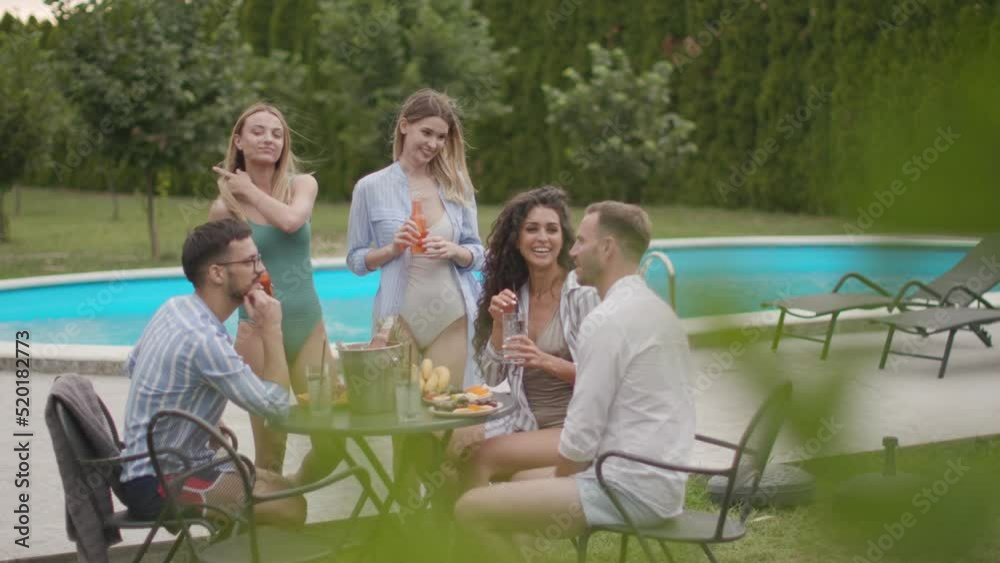 Group of happy young people cheering with drinks and eating fruits by the pool in the garden Group of happy young people cheering with drinks and eating fruits by the pool in the garden