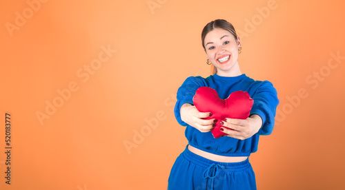 Beautiful woman holding a red heart. Orange background. 20-22 years old caucasian woman. © Maxim Morales