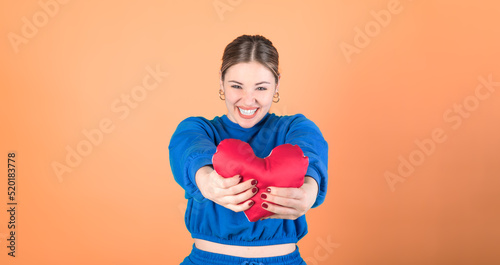 Beautiful woman holding a red heart. Orange background. 20-22 years old caucasian woman. © Maxim Morales