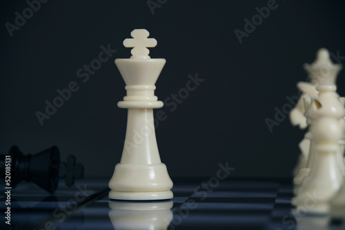 Standing white chess pieces and lying black king.