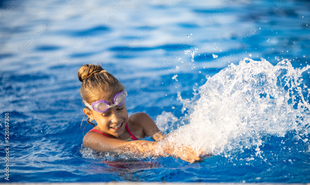 A girl with swimming goggles jumps into a pool with clear water on the background of a warm summer sunny sunset