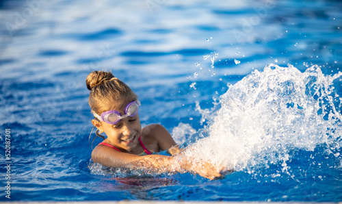 A girl with swimming goggles jumps into a pool with clear water on the background of a warm summer sunny sunset © YouraPechkin