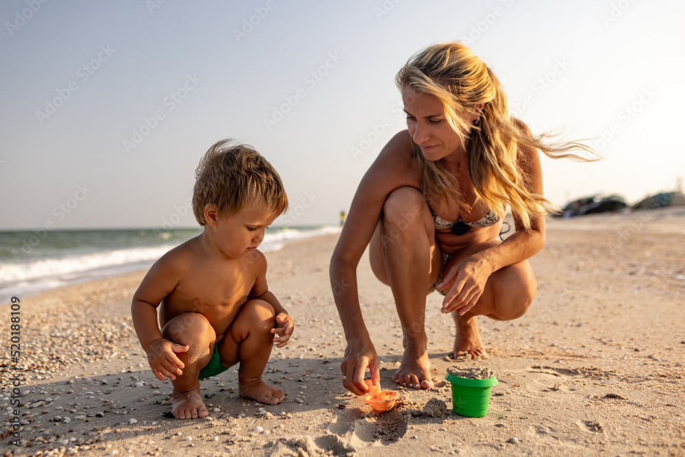 The kid collects shells and pebbles in the sea on a sandy bottom with his mother under the summer sun on vacation The kid collects shells and pebbles in the sea on a sandy bottom with his mother under the summer sun on vacation
