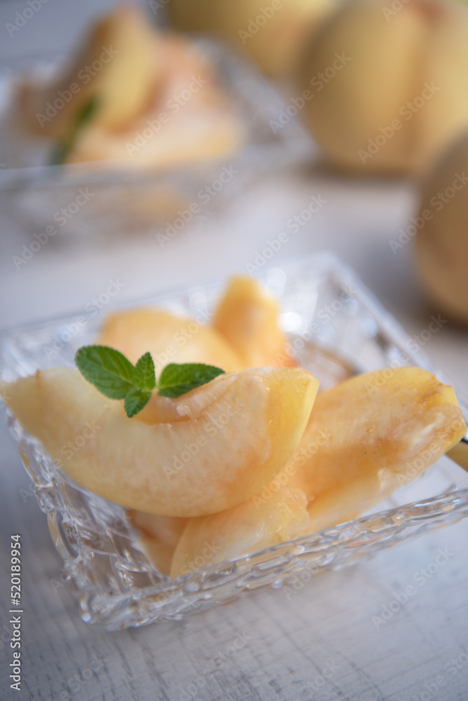 Pieces of japanese white peach in glass bowl on wooden background.