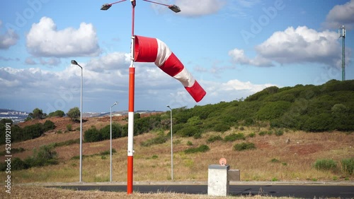 Wind sock fly. Summer hot day on private sporty airport with abandoned windsock, wind is blowing and windsock is lazy moving. Windsock with cloud sky mountain and road with cars on background  photo