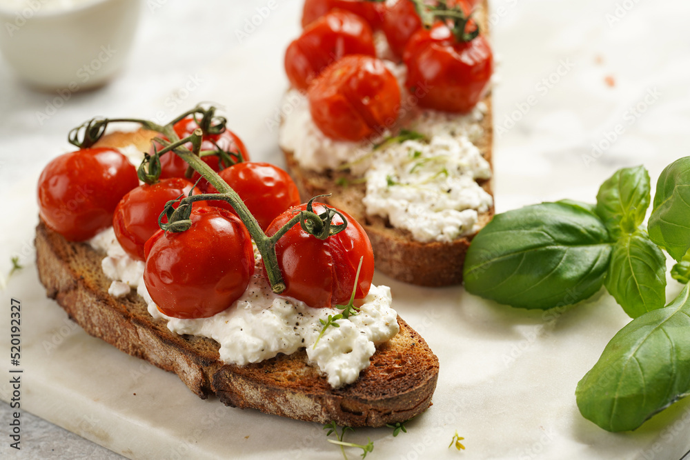 A sandwich with roasted cherry tomatoes with branch, fresh cottage cheese, green basil on a slice of whole wheat bread on a marble board on grey background A sandwich with roasted cherry tomatoes with branch, fresh cottage cheese, green basil on a slice of whole wheat bread on a marble board on grey background