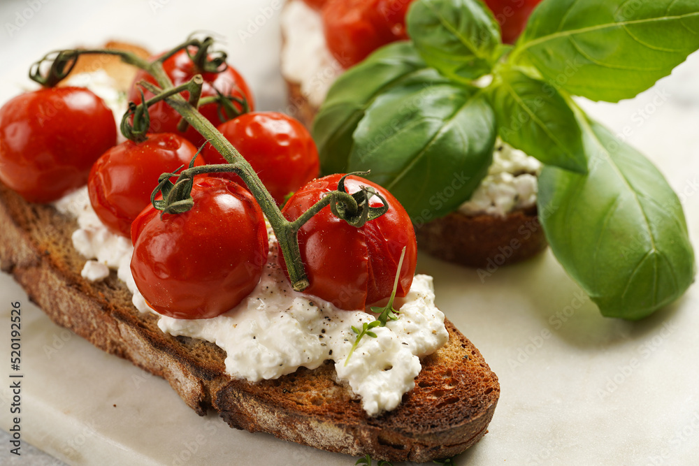 A sandwich with roasted cherry tomatoes with branch, fresh cottage cheese, green basil on a slice of whole wheat bread on a marble board on grey background A sandwich with roasted cherry tomatoes with branch, fresh cottage cheese, green basil on a slice of whole wheat bread on a marble board on grey background