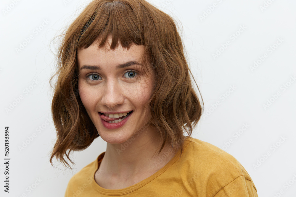 horizontal close-up portrait of a beautiful, playful woman in a yellow T-shirt on a light background amusingly showing her tongue to the camera horizontal close-up portrait of a beautiful, playful woman in a yellow T-shirt on a light background amusingly showing her tongue to the camera