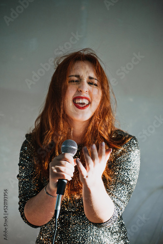 Portrait of redhead female singer woman in sparkly evening dress holding microphone