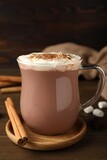 Glass cup of hot cocoa with whipped cream and aromatic cinnamon on wooden table