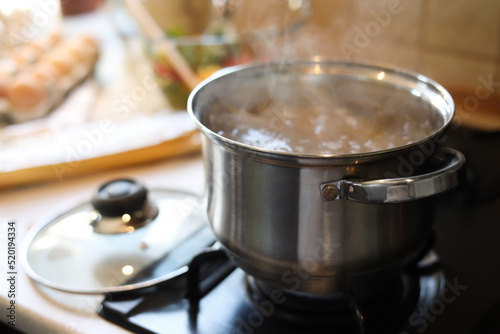 Shiny pot with boiling water on stove indoors. Space for text