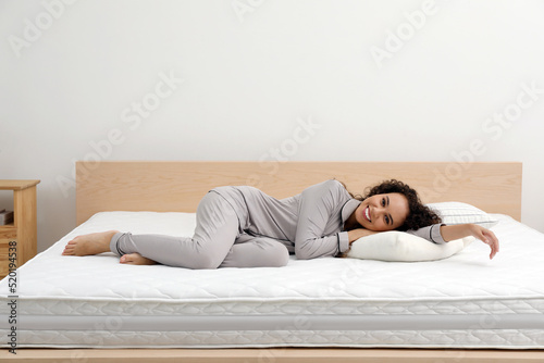 Happy young African American woman on bed with comfortable mattress and pillow at home © New Africa