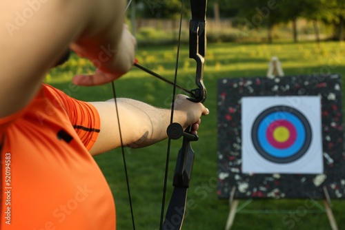 Man with bow and arrow aiming at archery target in park, closeup photo