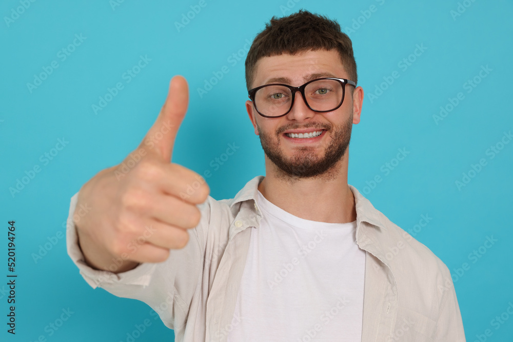 Young man showing thumb up on light blue background Young man showing thumb up on light blue background