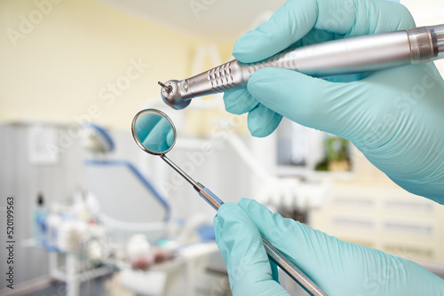 Dentist s hands in gloves with dental handpiece and mouth mirror.