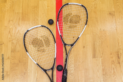 Two rackets and two squash balls lie on the parquet floor © ribalka yuli