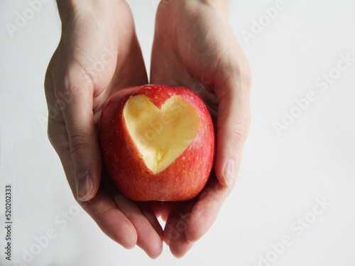 Fototapeta Naklejka Na Ścianę i Meble -  Male hands holding an apple, cut in the shape of a heart on a white background. Apples are excellent for heart health. Those who consume apples have less risk of having cardiovascular problems.