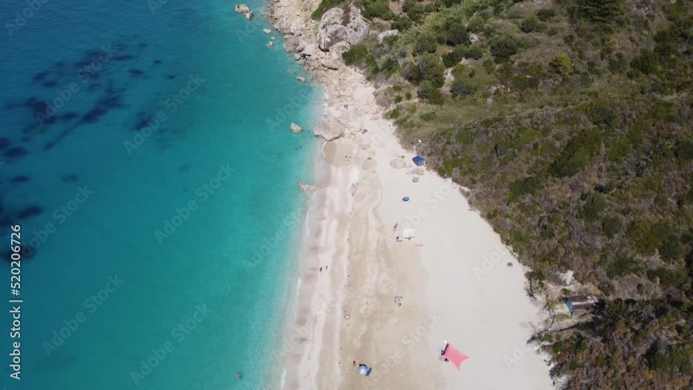 Aerial view of beautiful sandy beach with sunshades and soft turquoise ocean wave. Tropical sea in summer season on Megali Petra beach on Lefkada island.