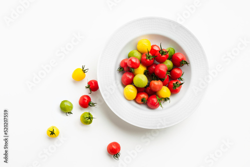 Colorful cherry tomatoes in organic red, yellow and green are served on a white round plate. The concept is to eat ripe vegetables neatly. Vegetarian diet space, flat top view.