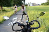 Kierownica roweru, para ludzi jedzie na rowerach ścieżką rowerową.