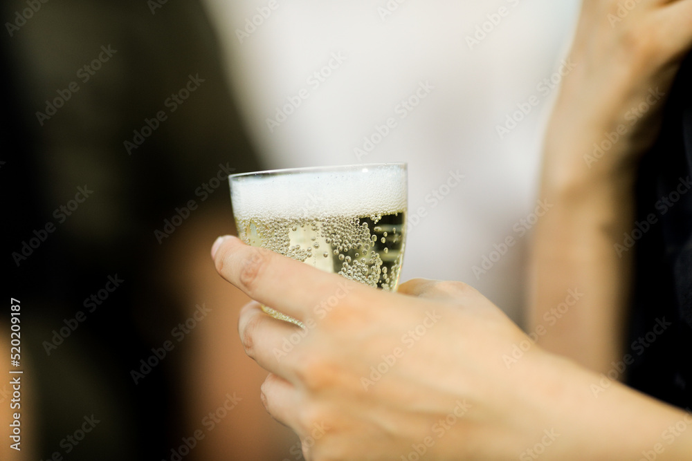 Shallow depth of field (selective focus) details with the hand of a woman holding a plastic glass of champagne or sparkling wine. Shallow depth of field (selective focus) details with the hand of a woman holding a plastic glass of champagne or sparkling wine.