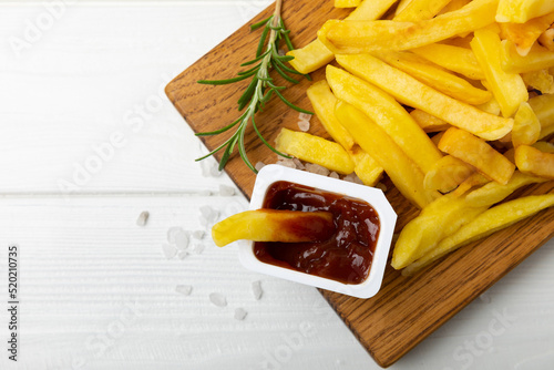 French fries with ketchup tomato sauce on a wooden background. Fast food. Baked homemade potatoes with rosemary. Harmful food. Place for text. Copy space.