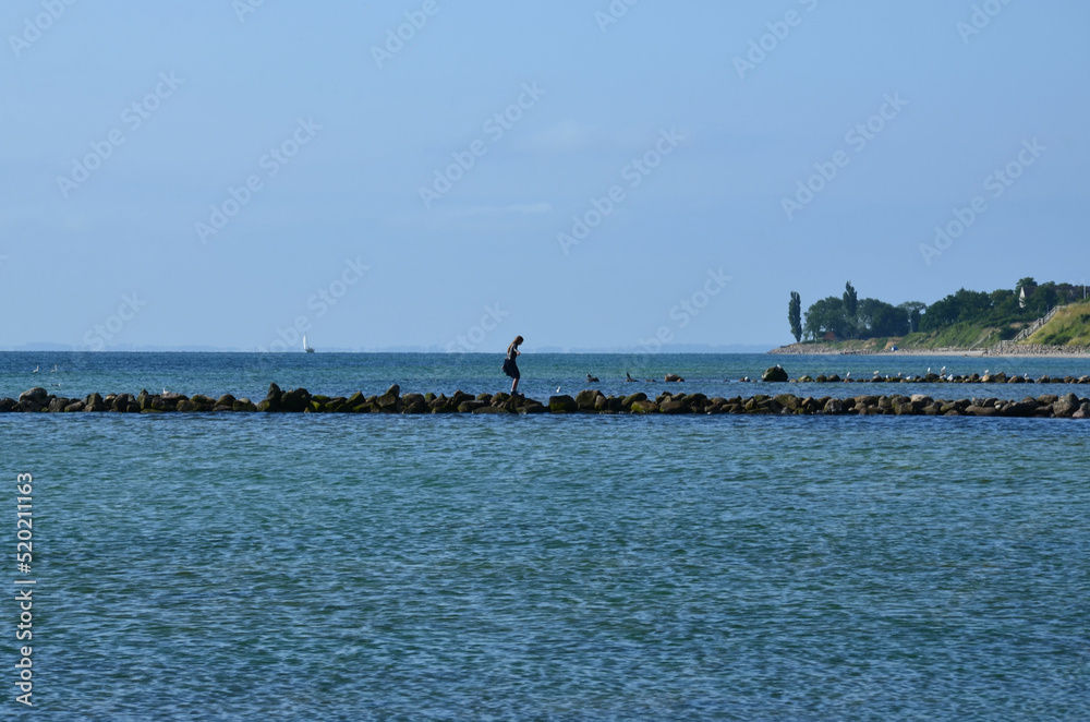 Frau klettert auf Felsen zum Küstenschutz der Ostsee
