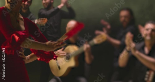 Beautiful stylish female artist dancing spanish style dance . Group of men playing on guitar and applauds to the dancer woman . Concept footage of spanish traditional culture . Waving cloth of skirt