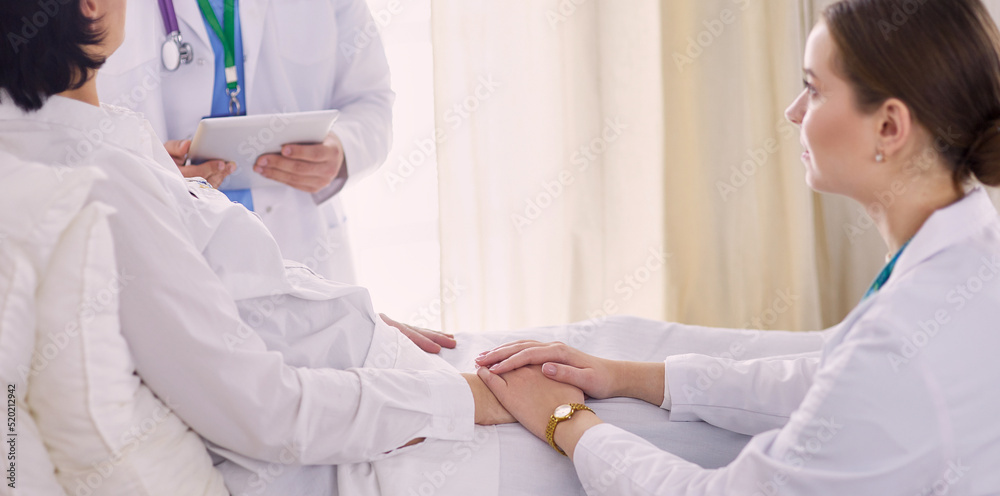 medical doctor holing senior patient's hands and comforting her