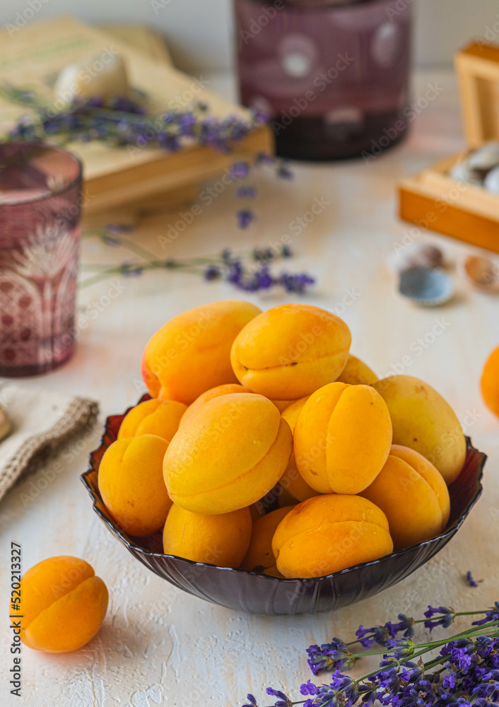 Ripe juicy apricots in a burgundy glass bowl on a light concrete background. Vintage style.