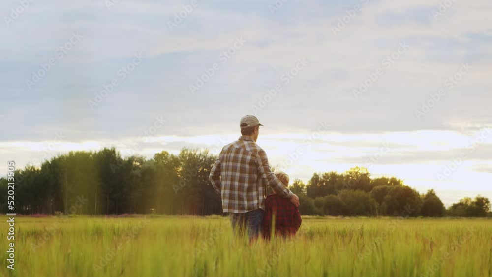 Farmer and his son in front of a sunset agricultural landscape. Man and a boy in a countryside field. Fatherhood, country life, farming and country lifestyle concept.