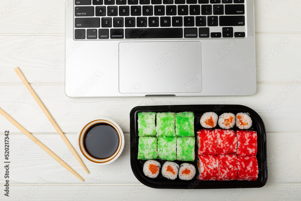 Office work, lunches and home delivery. Seafood sushi set on white table with laptop and blank screen. Food delivery concept.Japanese food.Copy space. Place for text. Office work, lunches and home delivery. Seafood sushi set on white table with laptop and blank screen. Food delivery concept.Japanese food.Copy space. Place for text.