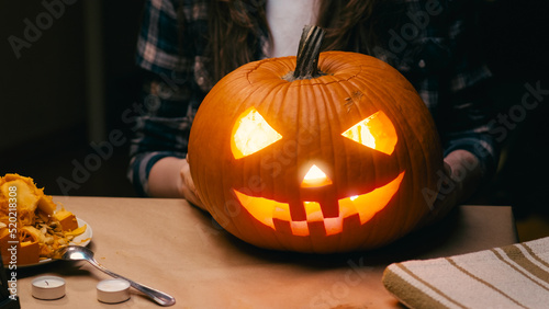 Illuminated pumpkin for Halloween. Woman sitting and showing out candle lit halloween Jack O Lantern pumpkin at home for her family.