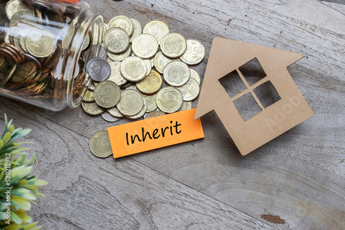 INHERIT was written on the post-it note with a house model and pile of coins flowing from the glass jar