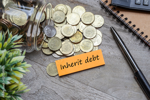 Valokuva INHERIT DEBT message on the post-it note on the pile of coins flowing from the g