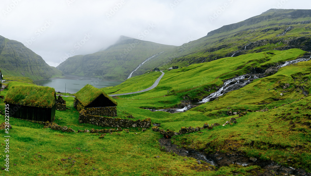 Obraz premium Panoramic view of waterfall running into the lake on the black beach in an old village named Saksun in Faroe islands which is a part of Denmark on a cloudy day